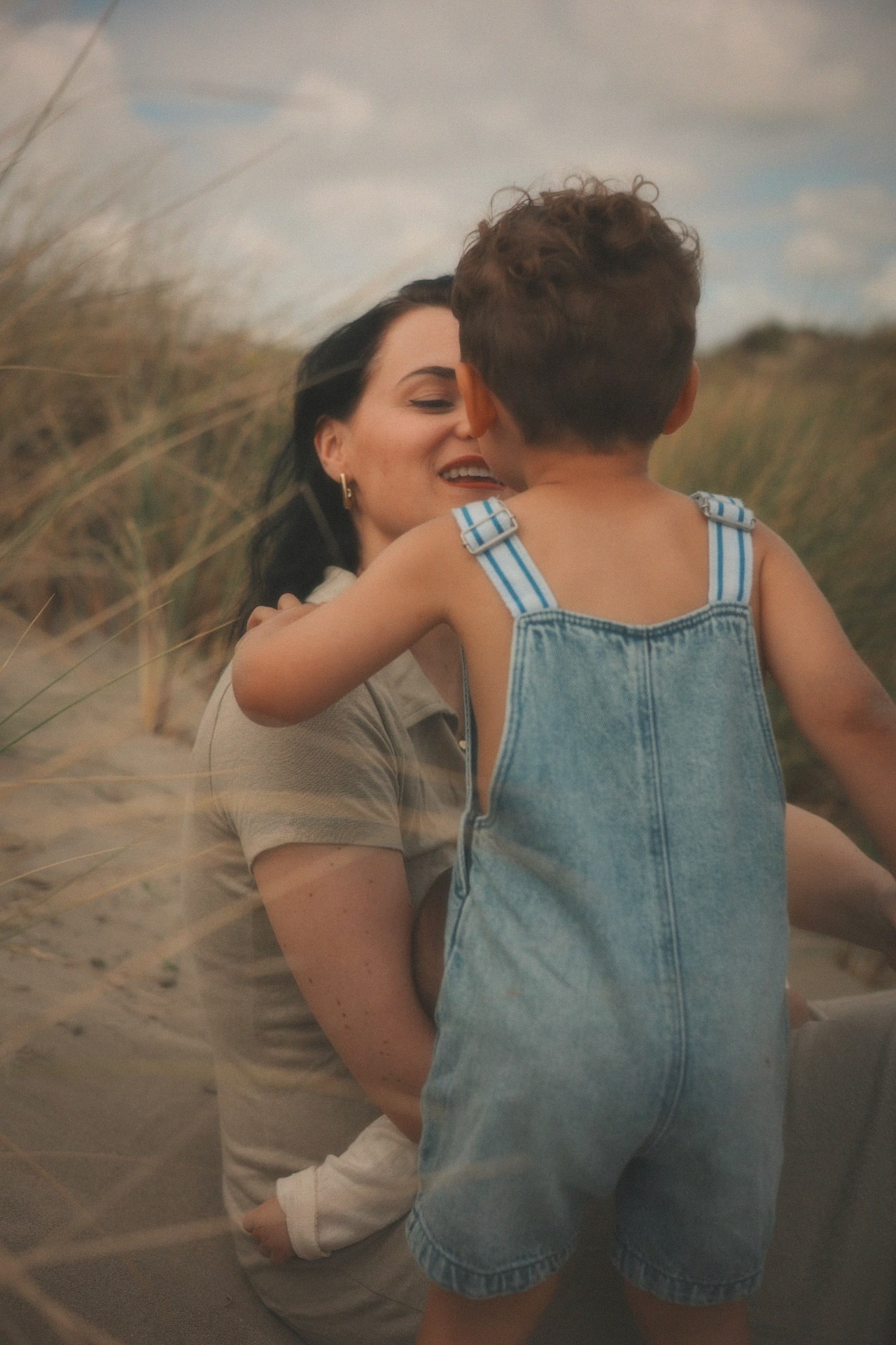 Moeder lacht tegen haar zoontje in de duinen