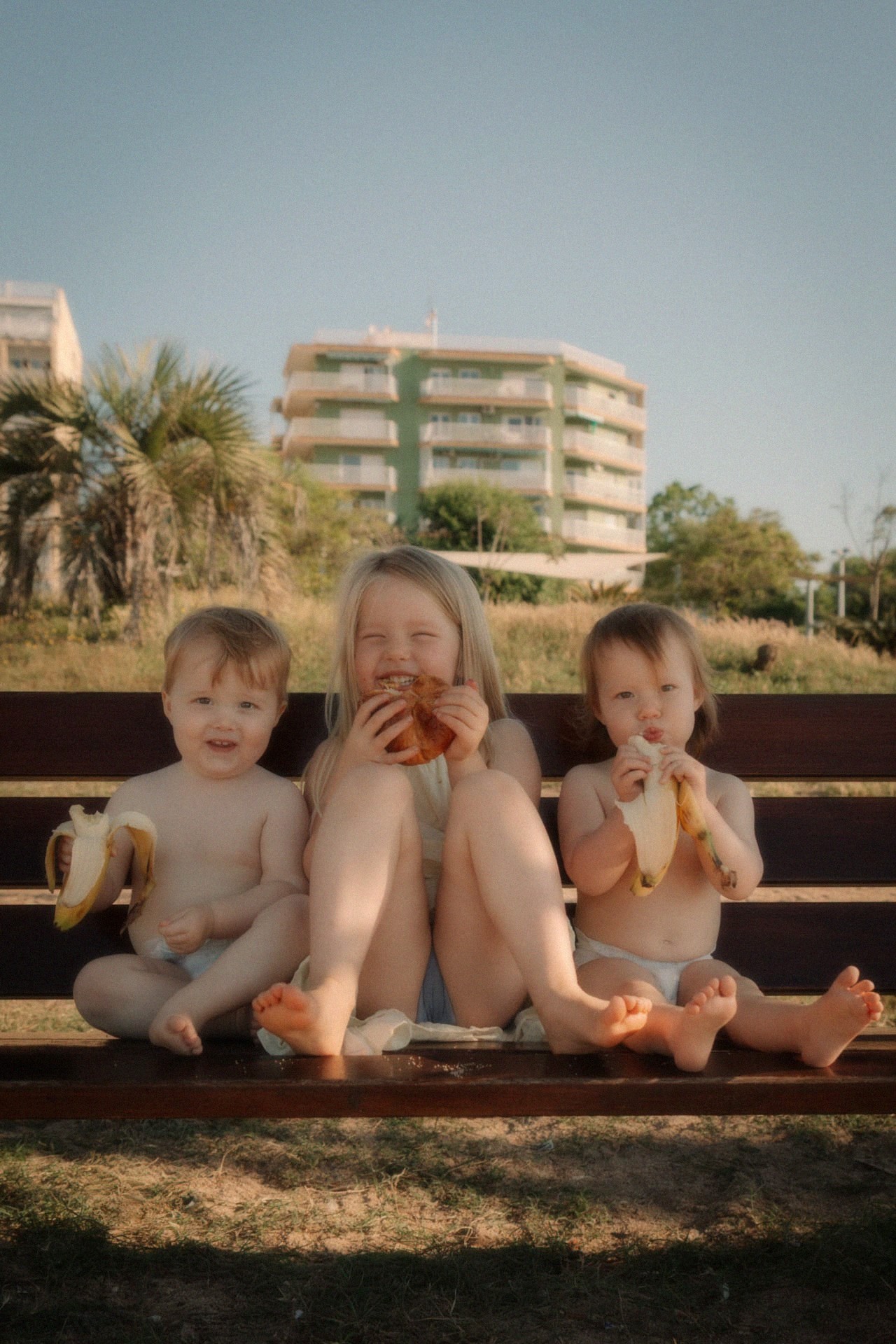 Drie kinderen eten fruit op een bankje in de zon