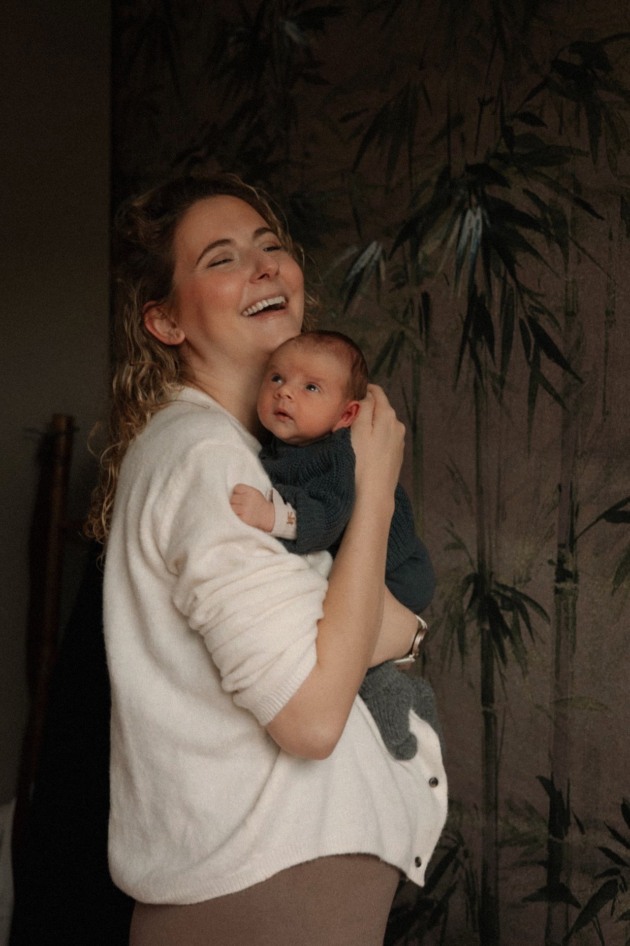 Moeder lacht vol overgave met haar newborn tegen zich aan