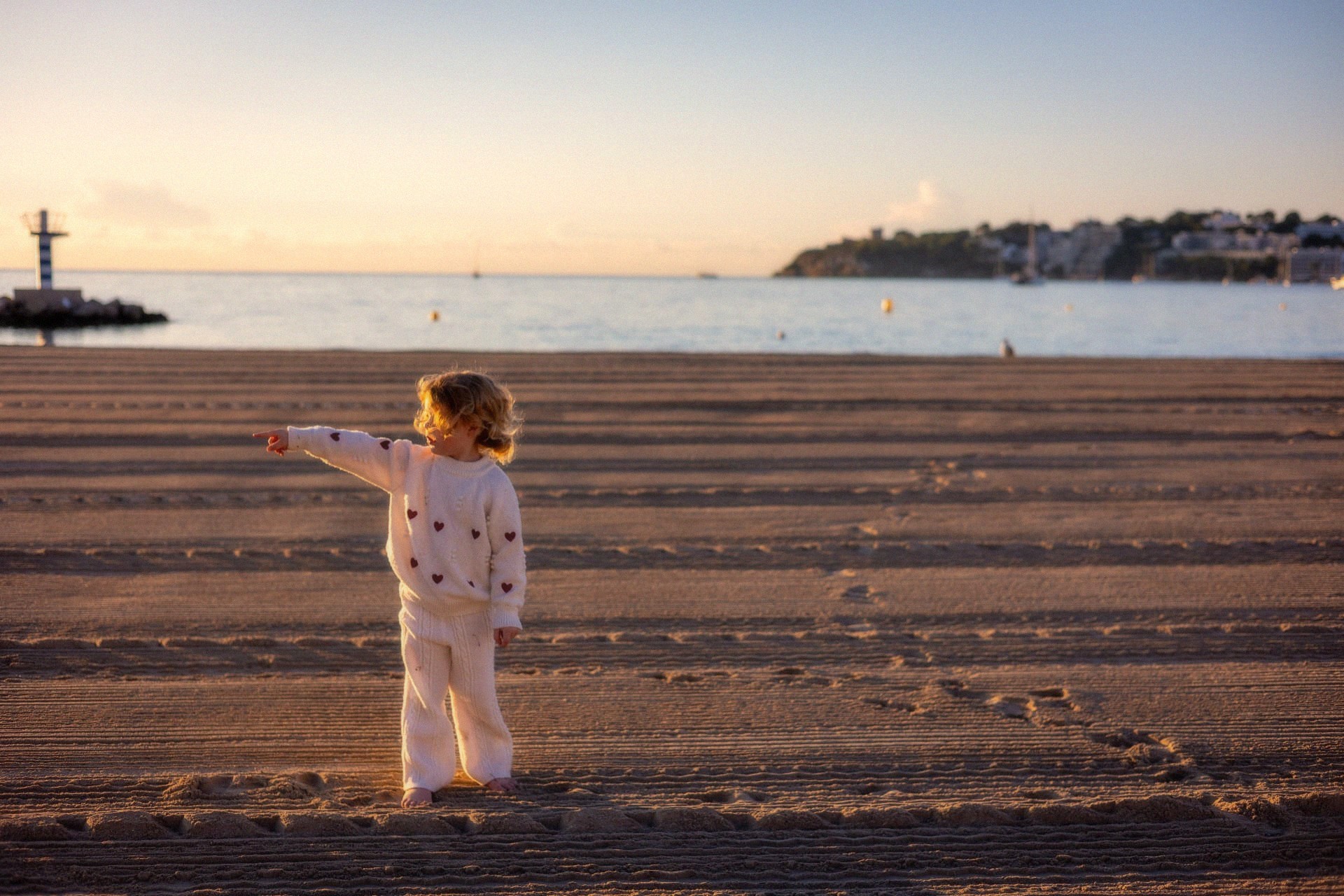 Meisje wijst naar de zee op een leeg strand in ochtendlicht